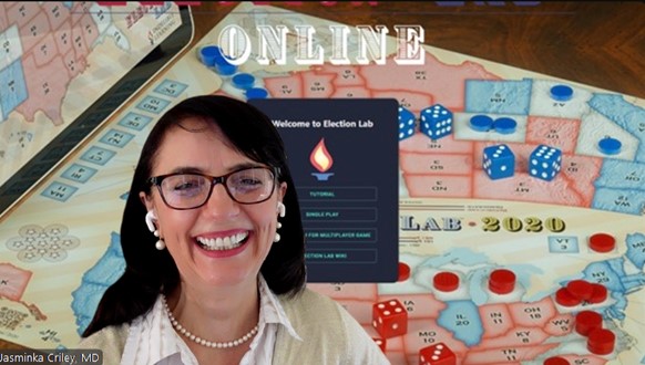 Dr. Jasminka Criley smiling during a video call while presenting Election Lab Online, with a U.S. election-themed board game and dice visible in the background.
