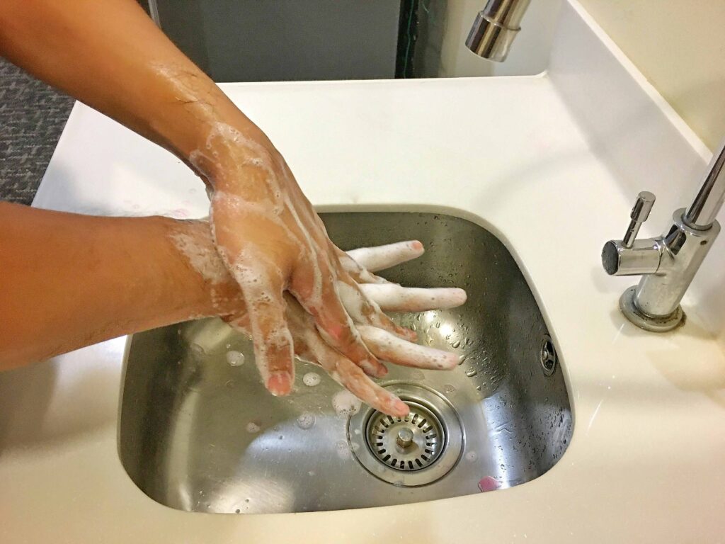 Person demonstrating proper handwashing technique at a sink, rubbing the left palm over the back of the right hand.